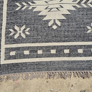 May include: Black and white patterned rug with a fringe border. The rug has a geometric design with arrows and stars.