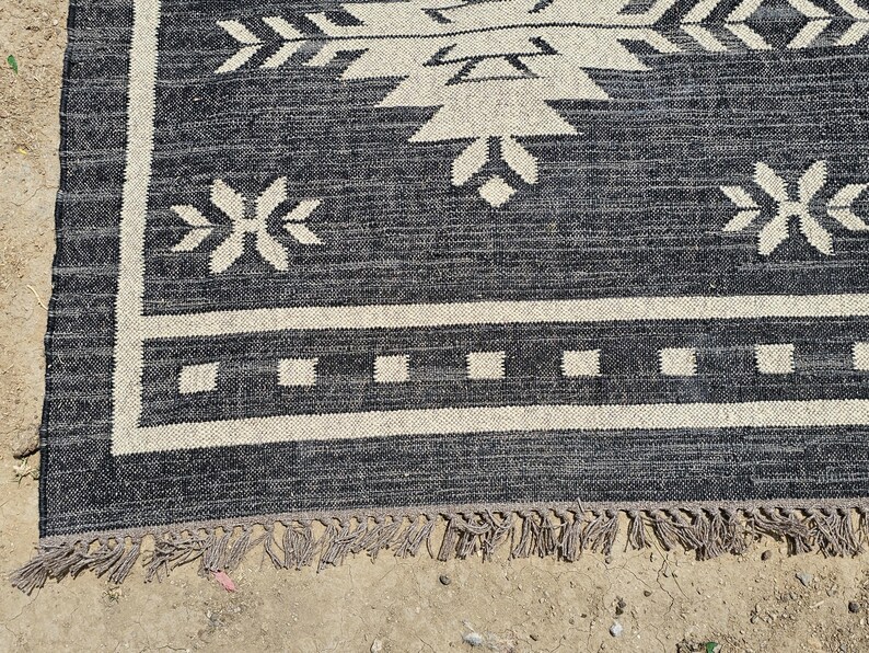 May include: Black and white patterned rug with a fringe border. The rug has a geometric design with arrows and stars.