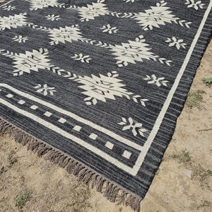 May include: Black and white patterned rug with fringe. The rug has a geometric design with white stars and diamonds on a black background.