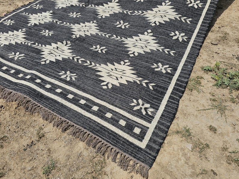 May include: Black and white patterned rug with fringe. The rug has a geometric design with white stars and diamonds on a black background.
