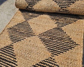 May include: A natural jute runner rug with a geometric diamond pattern in black and tan. The rug is partially rolled up, showcasing the texture and design. Ideal for adding a rustic touch to any space.