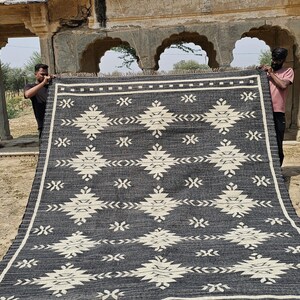 May include: A black and white handwoven rug with a geometric pattern. The rug is made of natural fibers and has a fringed edge.