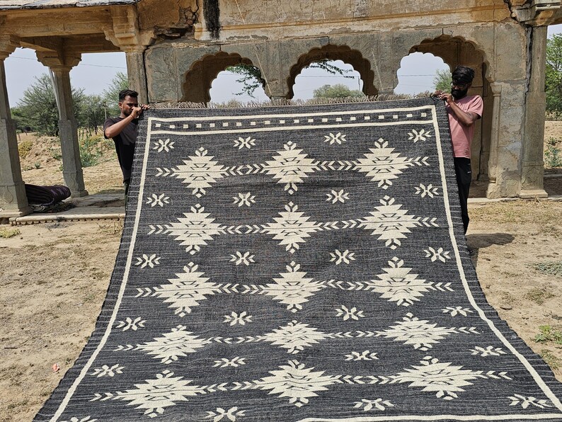 May include: A black and white handwoven rug with a geometric pattern. The rug is made of natural fibers and has a fringed edge.