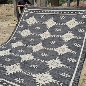 May include: Black and white rug with a geometric pattern. The rug is made of a woven material and has a fringed edge.