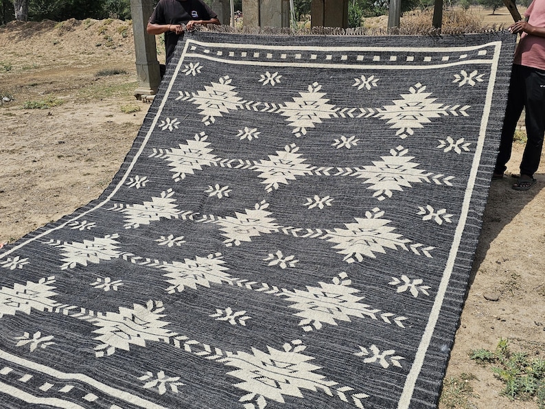 May include: Black and white rug with a geometric pattern. The rug is made of a woven material and has a fringed edge.