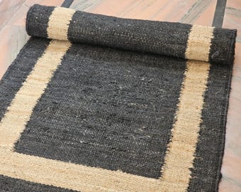 May include: A rolled-up, rectangular jute rug with a dark gray center and a natural beige border. The rug is made of woven fibers, creating a textured surface. The border frames the rug's central area.