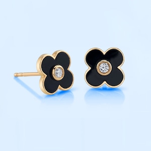 May include: A pair of gold earrings with black enamel flower designs and a small diamond in the center of each flower.