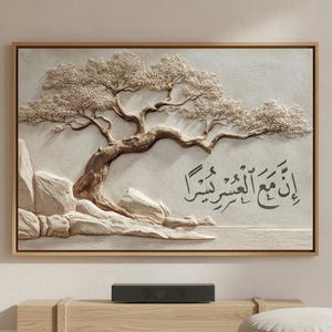 May include: A framed, textured artwork featuring a detailed relief of a tree with a winding trunk and textured leaves. The artwork is in neutral tones, with the tree and rocks in shades of beige and brown. Arabic calligraphy is included.
