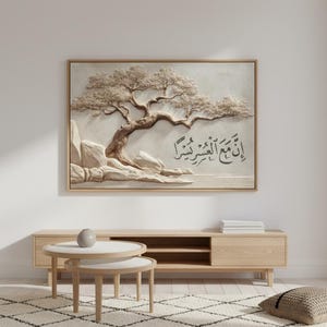 May include: A framed artwork featuring a 3D relief of a tree with text in Arabic script. The artwork is in neutral tones, with a light beige background and a wooden frame. The tree's branches and leaves are detailed, and the text is in black.