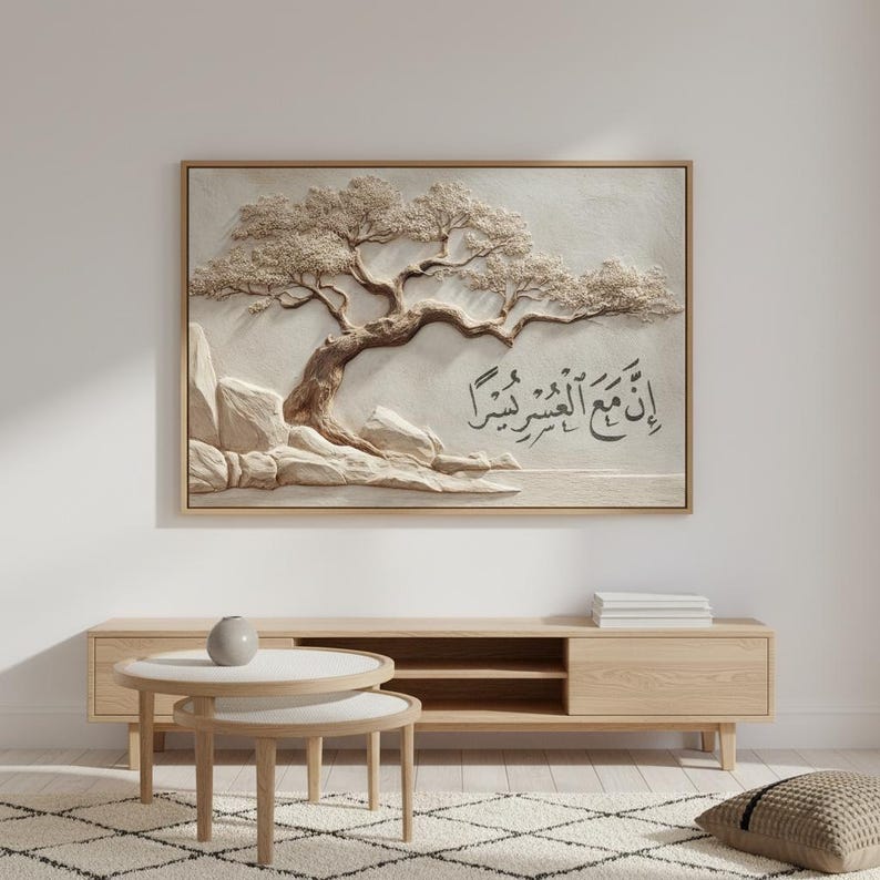 May include: A framed artwork featuring a 3D relief of a tree with text in Arabic script. The artwork is in neutral tones, with a light beige background and a wooden frame. The tree's branches and leaves are detailed, and the text is in black.