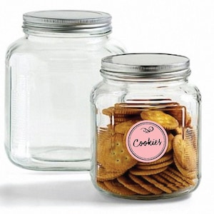 May include: Two glass jars with silver lids. The jar on the right is filled with cookies and has a pink label that says "Cookies" with a decorative swirl.