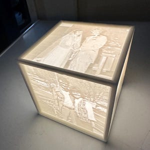 May include: A white cube-shaped lamp with a 3D image of a couple on their wedding day. The image is illuminated from behind, creating a soft glow.