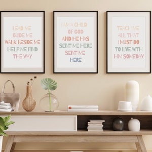 May include: Three framed prints with inspirational text in a light pink, light blue, and light green color scheme. The text on the prints reads: "Lead me, Guide me, Walk beside me, Help me find the way", "I am a child of God, and he has sent me here, sent me here", and "Teach me all that I must do, to live with him someday".