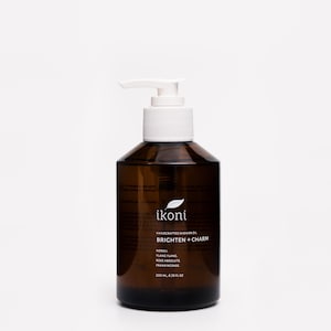 May include: A brown glass bottle of ikoni handcrafted shower oil with a white pump dispenser. The label reads "BRIGHTEN + CHARM" and lists ingredients. The bottle contains 6.76 fl oz (200 ml) of product.