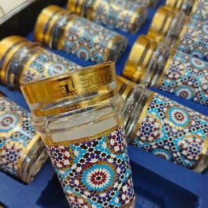 May include: A collection of clear glass tea cups featuring detailed mosaic patterns in blue, red, and gold. The rims and bases have gold trim. The cups are presented in a blue box, highlighting their decorative appeal.