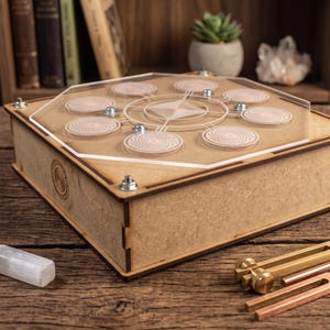 Puede incluir: Una caja cuadrada de madera con una tapa hexagonal de acrílico transparente que presenta patrones geométricos grabados y siete diseños de espirales circulares. La caja está asegurada con pernos metálicos e incluye un diapasón de latón.