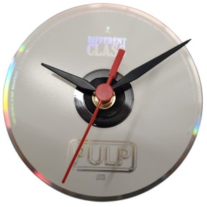 Puede incluir: Un reloj de vinilo blanco con agujas negras y rojas. El disco tiene el texto "DIFFERENT CLASS" y "PULP" impreso.