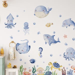 May include: Watercolor wall decals featuring various sea creatures, including a whale, shark, octopus, and seahorse. The decals are in shades of blue, yellow, and green, with bubbles and aquatic plants. The design is suitable for a child's room or bathroom.