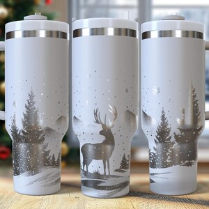 May include: Three white insulated travel mugs with silver detailing and handles. Each mug has a winter scene with a deer or trees in a snowy landscape. The mugs are on a wooden surface.