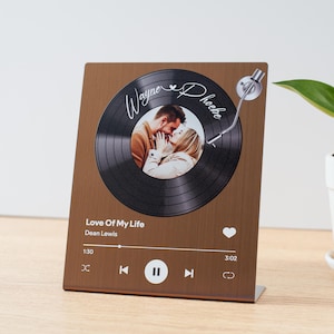 May include: A rectangular bronze-colored metal plaque featuring a graphic of a black vinyl record with a central photograph of a couple. The text reads Wayne and Phoebe, Love Of My Life, Dean Lewis, 1:30, and 3:02, with music player icons.
