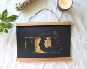 Könnte beinhalten: Ein schwarzer gerahmter Druck mit einem goldenen Foliendesign einer Person in einer Yoga-Pose. Die Pose ist über eine goldene Spirale gelegt, die eine Darstellung der Fibonacci-Sequenz ist. Der Druck hat den Text "Happy Joy" unten.