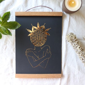 May include: A black framed print featuring a gold geometric design of a person hugging themself. The design resembles a flower or mandala.