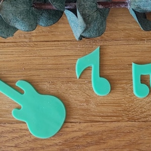 Könnte beinhalten: Hellgrüne Ausstanzungen in Form einer Gitarre und zweier Noten auf einer Holzoberfläche. Die Gitarre befindet sich links, mit einer Viertelnote und einer Achtelnote rechts. Eukalyptusblätter befinden sich oben.