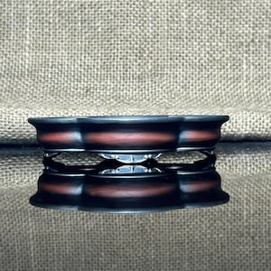 Könnte beinhalten: Ein dekoratives, mehrstöckiges, schwarz-rotes Gericht mit einem einzigartigen Design. Das Gericht hat eine dunkle Außenseite mit roter Innenseite und steht auf einer reflektierenden Oberfläche. Das Gericht wird wahrscheinlich zur Präsentation oder zum Servieren verwendet.