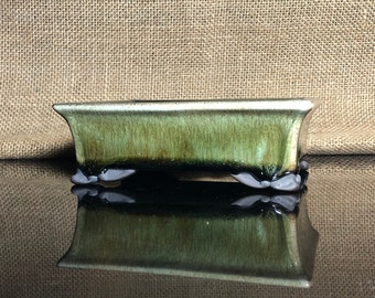 May include: A rectangular green glazed ceramic bonsai pot with a dark brown glaze on the bottom and four small feet. The pot is sitting on a black surface.