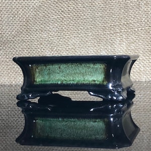 May include: A black rectangular bonsai pot with a green glaze and four legs. The pot is sitting on a black surface.