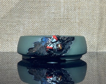 May include: A dark green ceramic bonsai pot with a black and silver glaze. The pot has a unique design with a raised, textured, black and silver design on the front. The design features a stylized, abstract shape with a red and white accent.