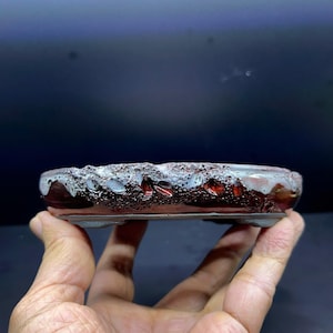 May include: A shallow, rectangular ceramic bonsai pot featuring a dark, glossy reddish-brown base with a textured, porous surface. The upper rim is finished with a thick, dripped white glaze that contrasts with the dark, earthy tones below.
