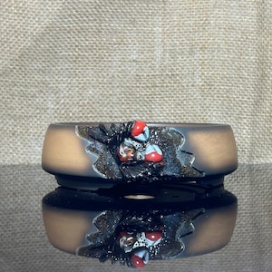 May include: A brown ceramic bonsai pot with a black and white design and red accents. The pot has a textured surface and a raised rim.