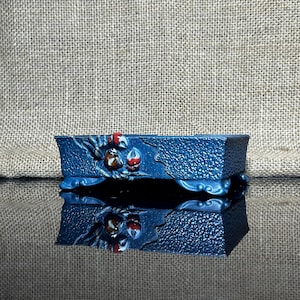 May include: A blue ceramic bonsai pot with a textured surface and a design of red and brown flowers. The pot has four legs and is sitting on a burlap surface.