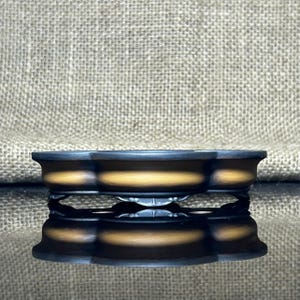 Puede incluir: Una bandeja decorativa de tres secciones, de color oscuro, con interior dorado, que descansa sobre un soporte de metal negro. El diseño de la bandeja se refleja en la superficie inferior. El fondo es una tela texturizada de color neutro.