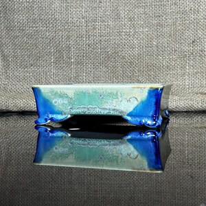 Op de afbeelding: Een rechthoekige bonsai pot van keramiek met een blauwe glazuur en een lichtgroen en wit gespikkeld ontwerp. De pot heeft vier kleine voetjes.
