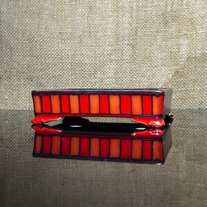 May include: A rectangular ceramic bonsai pot featuring a vibrant red and orange striped pattern with dark brown trim. The container is supported by four small, curved feet and has a glossy finish, reflecting light across its structured exterior surface.