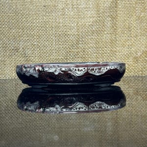 Könnte beinhalten: Ein flacher, ovaler Bonsai-Topf aus Keramik mit einer dunkelbraunen Grundglasur und einem kontrastierenden weißen Tropfglasur-Effekt am oberen Rand. Das Gefäß hat einen glatten, abgerundeten Rand und eine robuste Konstruktion für Pflanzen.