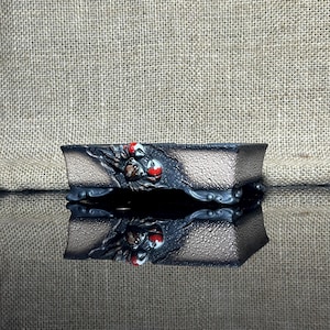 May include: A black and brown rectangular bonsai pot with a textured surface and a raised design of red and white flowers. The pot has a raised lip and four feet.