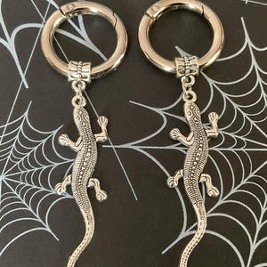 May include: Two silver keyrings with a lizard charm. Each keyring has a silver ring with a clasp.