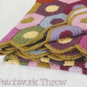 Puede incluir: Una manta patchwork plegada con una variedad de colores, incluyendo rosa, verde, morado y amarillo. La manta tiene un patrón hexagonal con un diseño circular en el centro de cada hexágono. El texto "Patchwork Throw" está en la parte inferior.