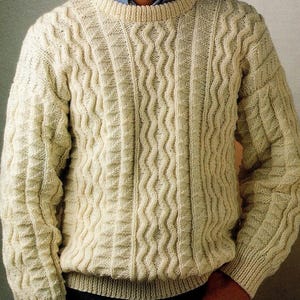 May include: Cream-coloured cable-knit jumper with a crew neck. The jumper features a textured pattern of vertical and wavy lines, creating a classic and warm look. The sleeves and body have a ribbed texture at the cuffs and hem.
