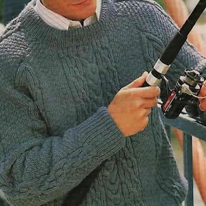 May include: A blue-gray cable-knit sweater with a crew neck and ribbed cuffs. The sweater has a textured pattern and is worn over a white collared shirt. The person is holding a fishing rod.