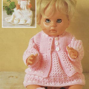 May include: A vintage doll with blonde hair and blue eyes, wearing a pink knitted outfit. The outfit includes a cardigan with white buttons, a dress, and matching booties. A smaller doll in a white knitted dress and bonnet is in the background.