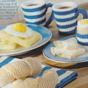 Puede incluir: Un juego de desayuno tejido a mano, que incluye una taza a rayas azules y blancas, un plato con un huevo frito, tostadas y un cruasán. El texto de la imagen dice: "No, no estás soñando: ¡este divertido 'desayuno' está hecho completamente de hilo!"