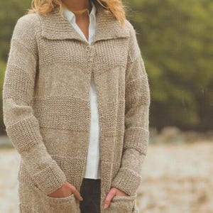 Peut inclure: Longue veste en tricot beige avec un col châle et deux poches avant. La veste est boutonnée en haut et portée sur une chemise blanche à col. Les manches sont longues et le style général est décontracté et confortable.