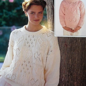 Può includere: Maglione lavorato a maglia color crema con motivi a rombi e foglie. Il maglione ha maniche lunghe e scollo tondo. Un'immagine più piccola mostra un maglione rosa con motivi simili. Esempi di maglieria.