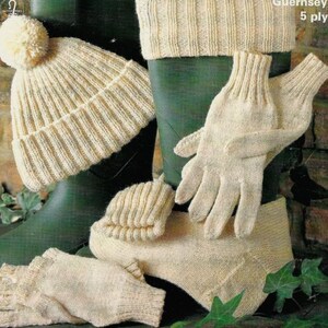 May include: A collection of cream-coloured knitted winter accessories, including a beanie with a pom-pom, gloves, socks, and a neck warmer, are displayed with green wellington boots. The text "Guernsey 5 ply" is visible.