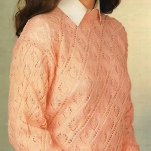 May include: A light peach-colored sweater with a diamond-patterned knit design. The sweater has long sleeves and a white collared shirt underneath. The knitwear is a soft, textured material, perfect for a cozy look.