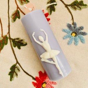 May include: A lavender candle with a white ballerina figurine on the front. The candle has a label that says "Candle Art".